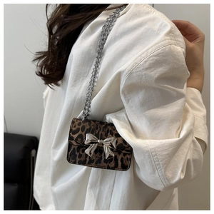 Detail of leopard print crossbody bag with silver metal bow and chain strap on model