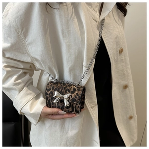 Detail of leopard print mini crossbody bag with a silver metal bow on a white shirt