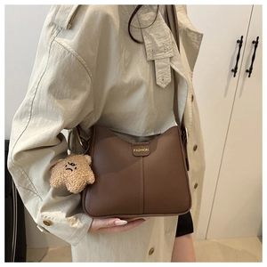 Détail d'un sac seau en cuir marron foncé avec logo doré et pendentif d'ours