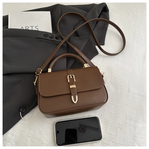 Detail view of vintage dark brown crossbody bag with gold buckle and a smartphone for scale