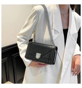 Dettaglio borsa a tracolla nera con cuciture geometriche e catena argento su blazer bianco