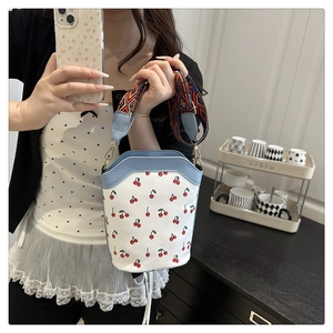 Detail of cherry print bucket bag with blue leather trim and colorful woven strap