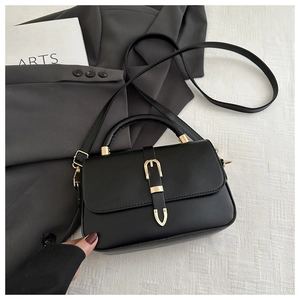 Close-up of black crossbody bag with golden buckle on a grey blazer background