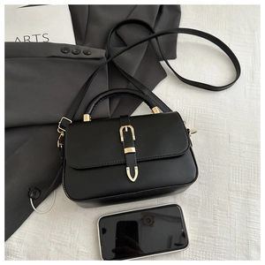 Close-up of black leather handbag with gold buckle shown next to a smartphone for scale
