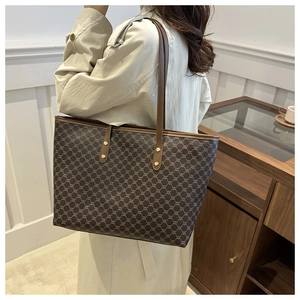 Detail of classic patterned tote bag with brown leather handles and gold-tone hardware