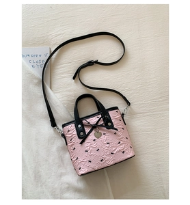 Dettaglio borsa a secchiello rosa con fiocchi e ciondolo a cuore su fondo bianco