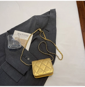 Detail of gold quilted mini crossbody bag with leather-threaded chain on suit jacket