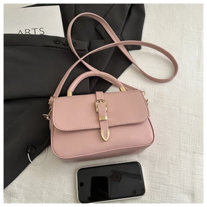 Pink faux leather handbag with gold belt buckle and top handle on a stylish background