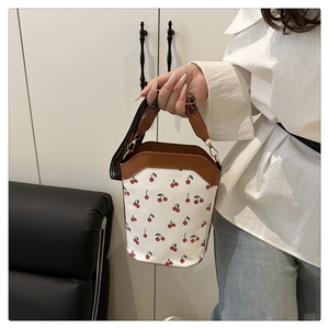 Detail of cherry print bucket bag featuring a colorful geometric woven wide shoulder strap