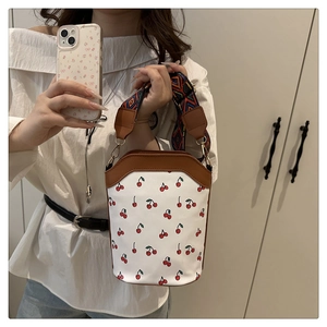Detail of cherry print bucket bag featuring brown leather trim and ethnic woven strap