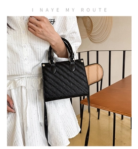 Detail of black woven leather tote bag featuring handcrafted texture and gold hardware
