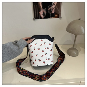 Detail of cherry print bucket bag featuring a colorful ethnic style wide woven strap