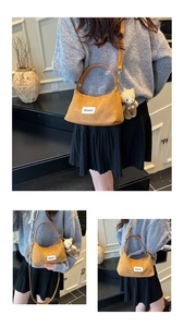 Detail of yellow corduroy handbag featuring a bear charm and adjustable shoulder strap