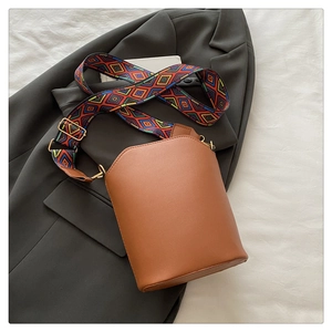 Close-up of brown leather bucket bag with geometric patterned fabric strap on grey blazer