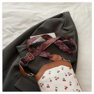 Detail of white canvas crossbody bag with red cherry print and brown leather trim features