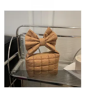 Detail of caramel puffer handbag featuring a large quilted bow handle and square stitching