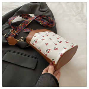 Detailed close-up of cherry print bucket bag with colorful woven shoulder strap and leather trim