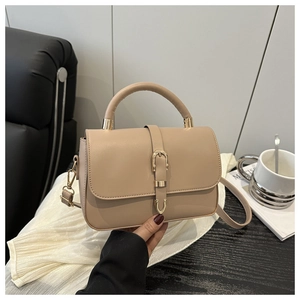 Detail of soft beige leather handbag with gold buckle on silk fabric background