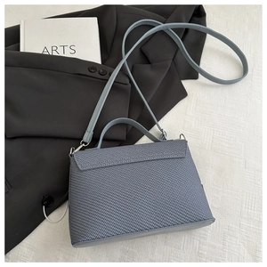 Dettaglio borsa blu con trama a croce su tessuto bianco con blazer nero e libro decorativo