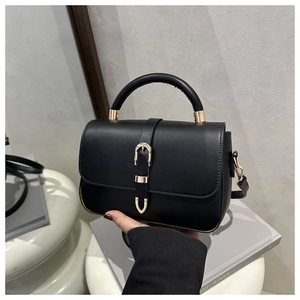 Detail of black leather handbag with round handle and gold buckle on a white stand
