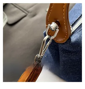 Macro view of blue denim handbag featuring brown leather handle and silver metal hardware