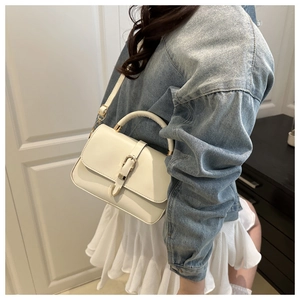 Detail of cream leather crossbody bag with U-shaped buckle on a model in denim jacket