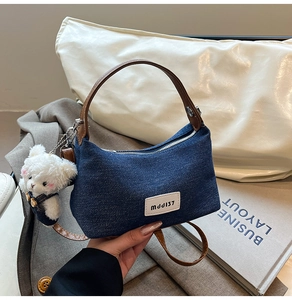Detail of dark blue denim handbag with brown leather handles and a plush bear pendant