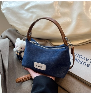 Detail of blue denim crossbody bag with brown leather handles and cute bear charm pendant