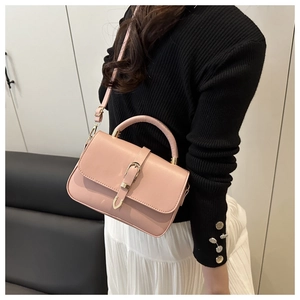 Close-up of pink leather crossbody bag featuring gold U-shaped buckle and slim shoulder strap