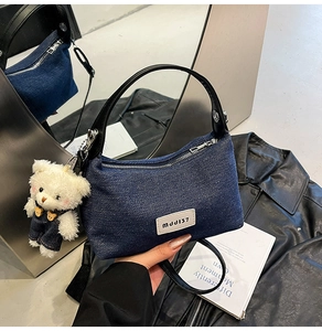 Detail of dark blue denim crescent bag with black leather handle and cute plush bear charm