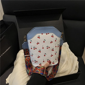 Fresh cherry print bucket bag in white with blue leather trim and geometric wide strap