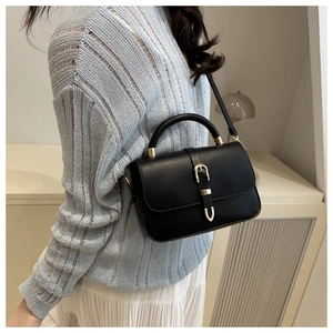 Detail of a black leather handbag with a golden horseshoe buckle on a light blue sweater