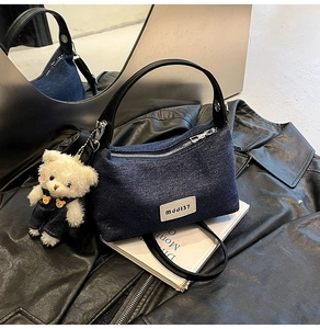 Detail of blue denim crossbody bag with leather strap and cute plush bear charm