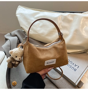 Detail of a brown textured crossbody bag with leather handles and a plush teddy bear charm