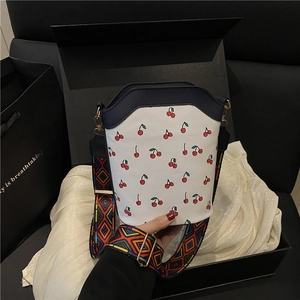 White cherry print bucket bag with colorful woven strap shown on elegant gift packaging