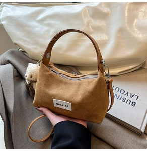 Detail of brown suede tote bag with white leather label and plush bear keychain
