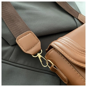 Dettaglio della borsa in pelle marrone con cuciture curve e chiusura a moschettone dorata