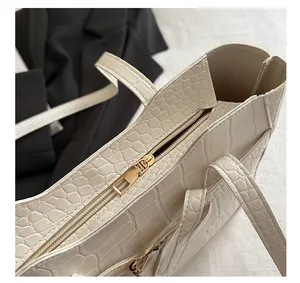 Close-up of cream tote bag featuring crocodile embossed texture and golden zipper detail
