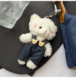 Plush bear keychain accessory with denim overalls and metal chain on a black fabric