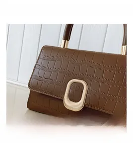 Detail of brown croc-embossed leather handbag with gold oval textured metal clasp