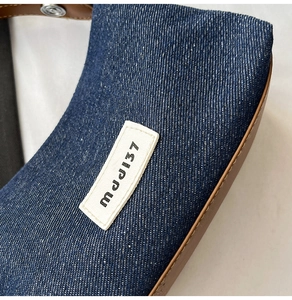 Close-up of denim fabric texture with white mjJ137 label and leather trim on handbag