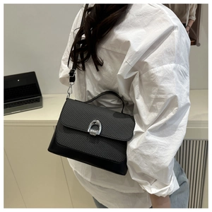 Dettaglio borsa nera in pelle intrecciata con fibbia argentata su camicia bianca