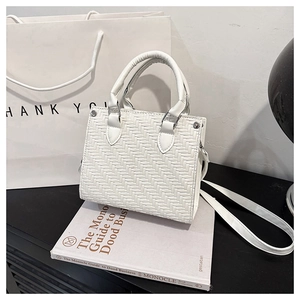 Close-up of white woven tote bag with silver hardware and detachable strap on books