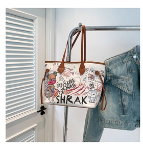 Detail of white graffiti tote bag with brown straps hanging next to a denim jacket