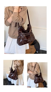 Detail of dark brown glossy tote bag with dual decorative buckles and a wide shoulder strap