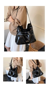Detail of glossy black hobo bag showing metallic buckle straps and patent finish texture