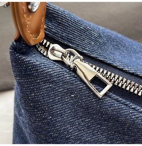 Detail of dark blue denim fabric with silver metal zipper and brown leather handle