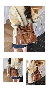 Detail of a brown glossy tote bag with dual metal buckles and shoulder strap view