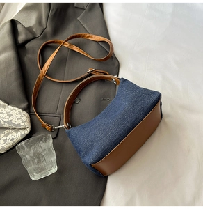 Close-up of retro denim handbag with brown leather trim and curved handles on grey fabric