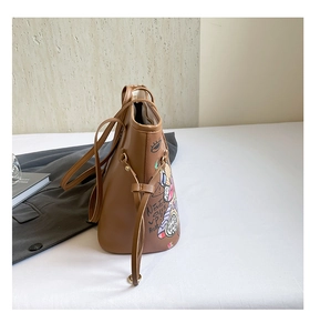 Detail of a brown tote bag featuring colorful graffiti prints and a secure zip closure